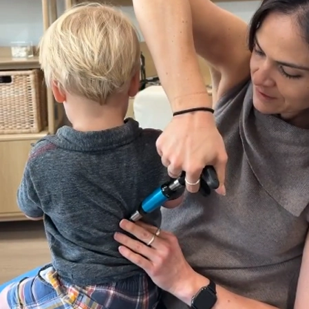 Dr. Ali Perez performing a gentle pediatric chiropractic adjustment using an instrument for targeted care.
